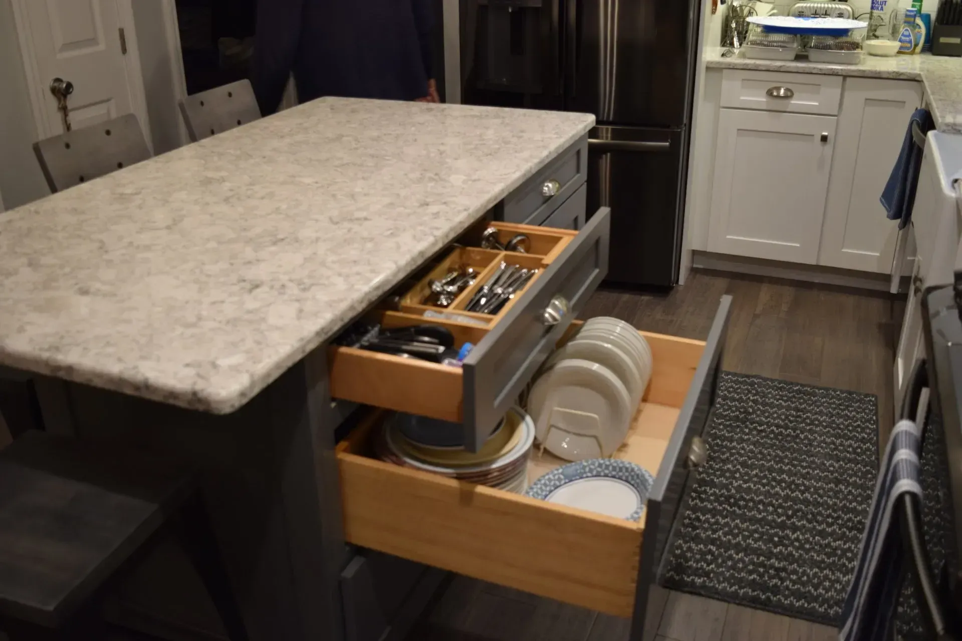 Kitchen island with open drawers revealing silverware and plates. Gray cabinets, light countertop.