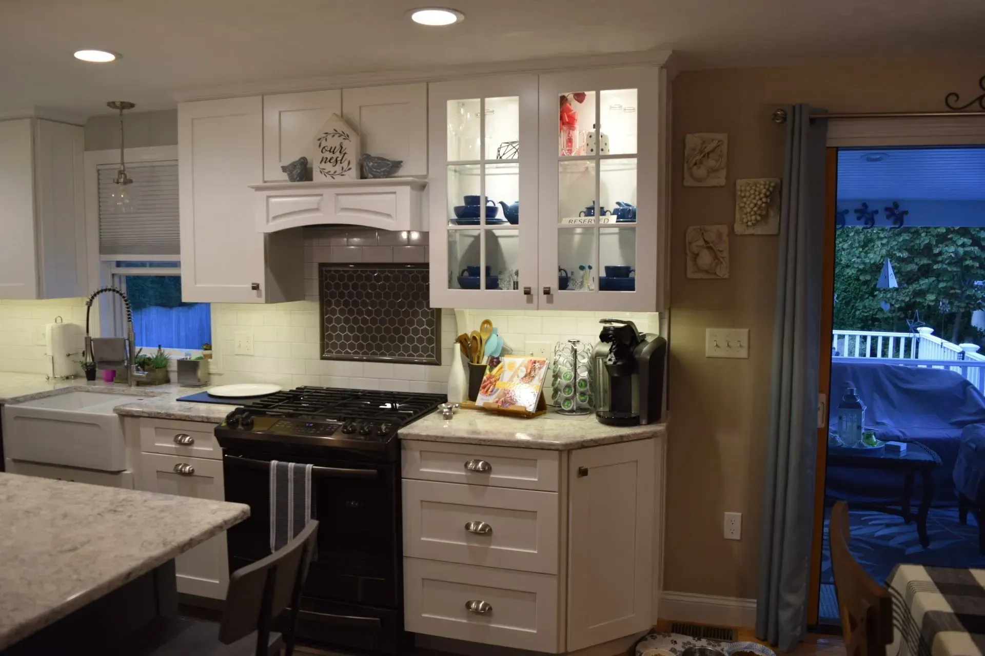 White kitchen with black range, light countertops, glass-door cabinet with blue dishware, and a door leading to a deck.