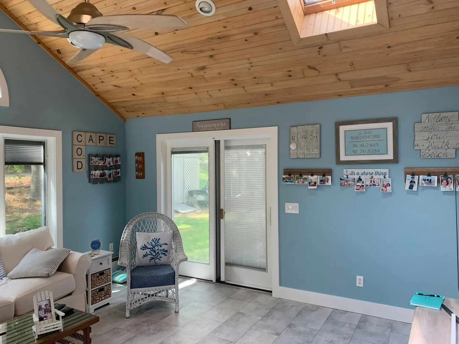 A sunroom with a wood ceiling, blue walls, a sliding door to a yard, and a wicker chair.