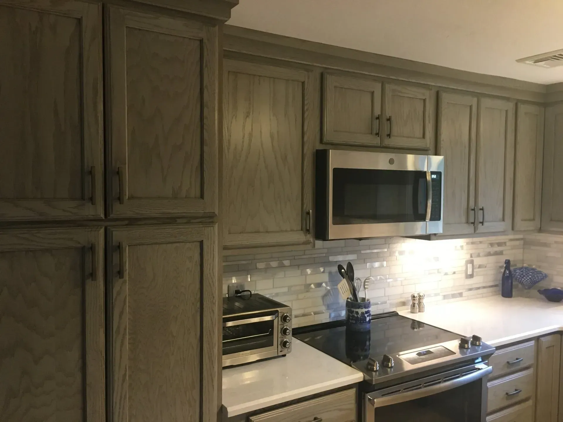 Kitchen cabinets, microwave, and appliances in a neutral-toned, modern style. White countertop and a tile backsplash.