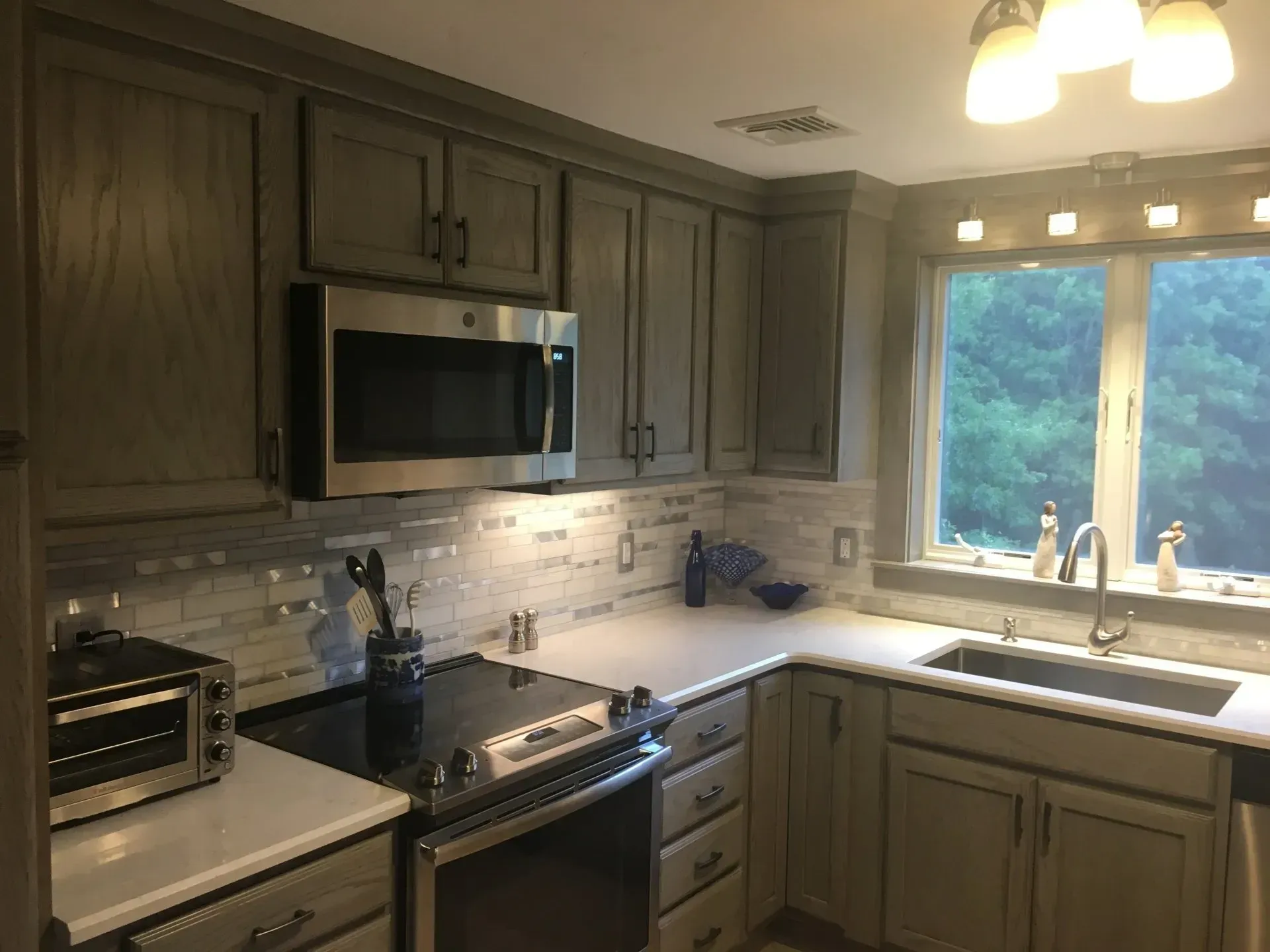 A renovated kitchen with gray cabinets, stainless steel appliances, and a window over a sink.
