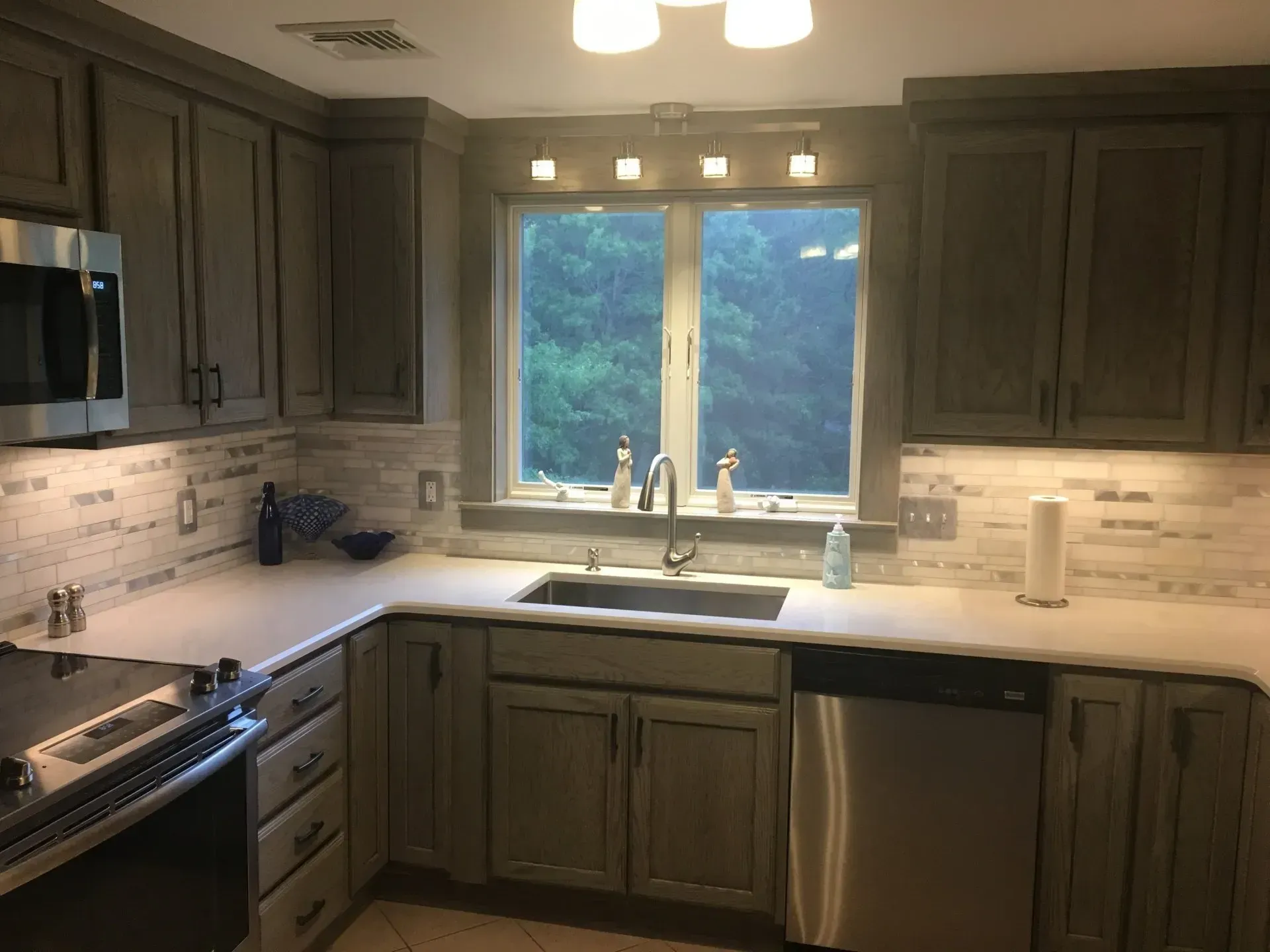 Kitchen with gray cabinets, white countertops, stainless steel appliances, and a window.