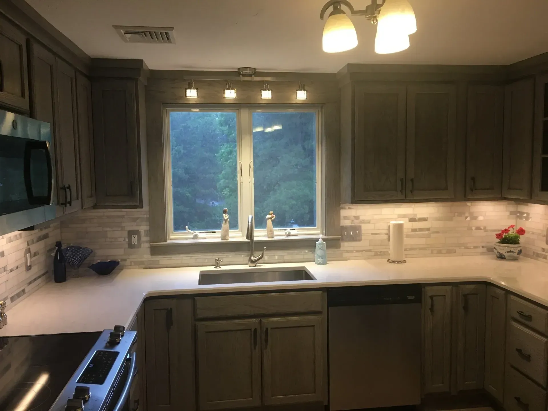 Kitchen with gray cabinets, white countertops, stainless steel appliances, and a window.