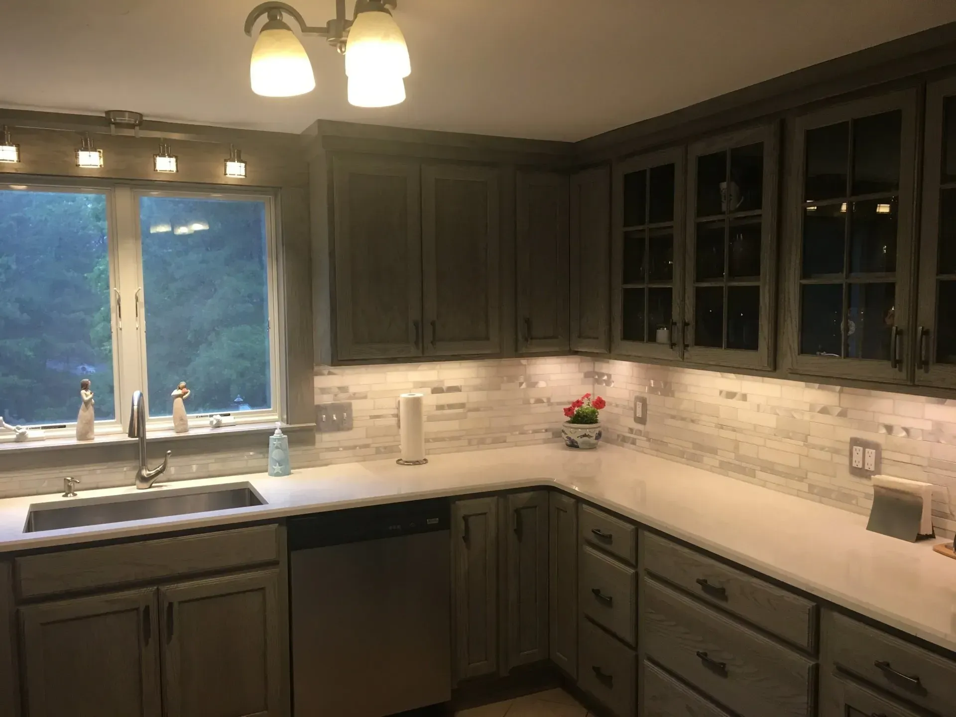 Gray kitchen with upper and lower cabinets, white countertops, and white brick backsplash.