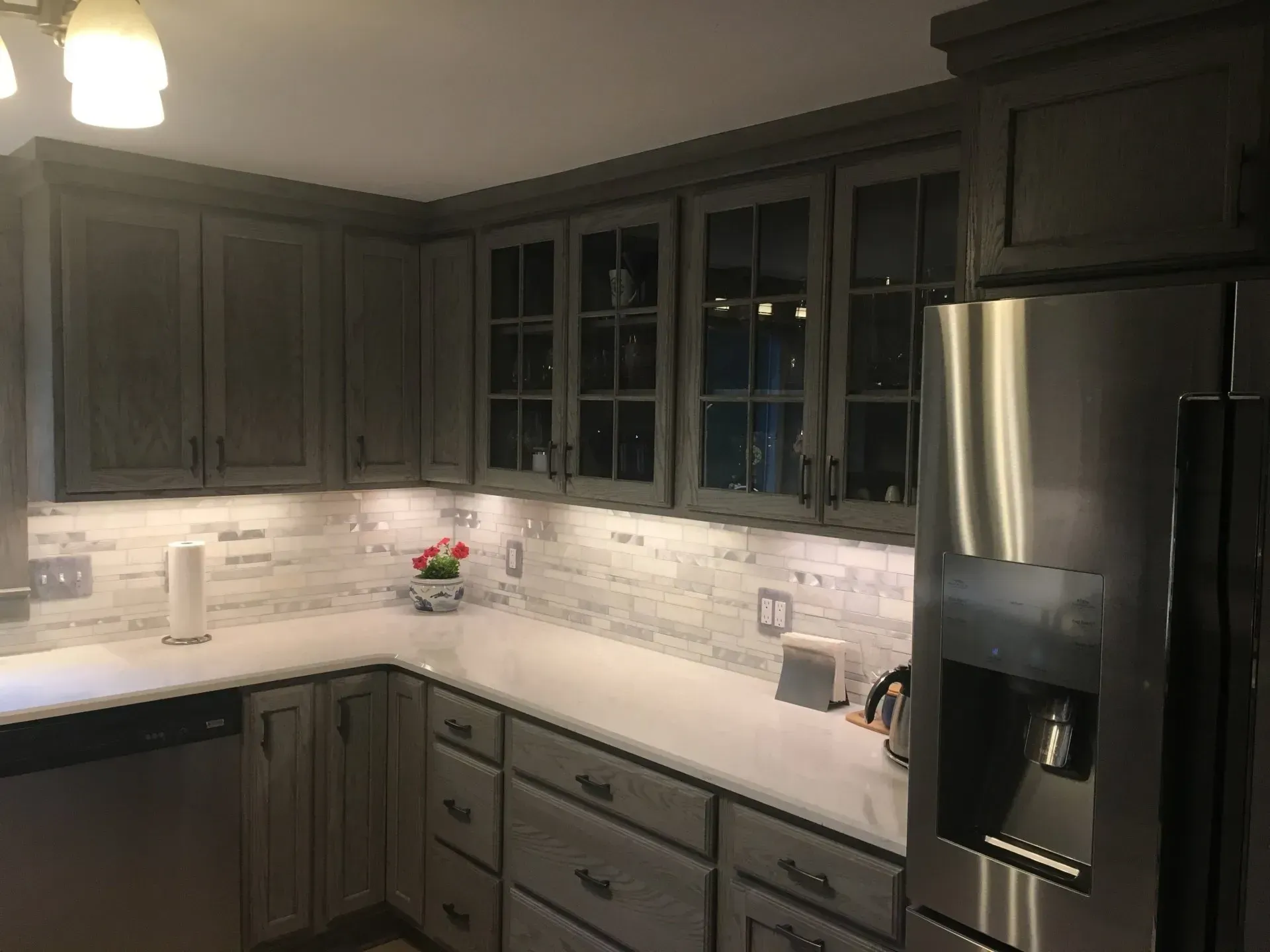 Kitchen with gray cabinets, white countertops, glass-front cabinets, and stainless steel refrigerator.