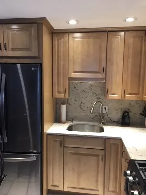 Kitchen with light wooden cabinets, stainless steel refrigerator, and sink.
