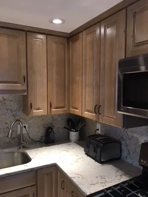 Kitchen corner with light wood cabinets, stainless steel appliances, and gray countertops.