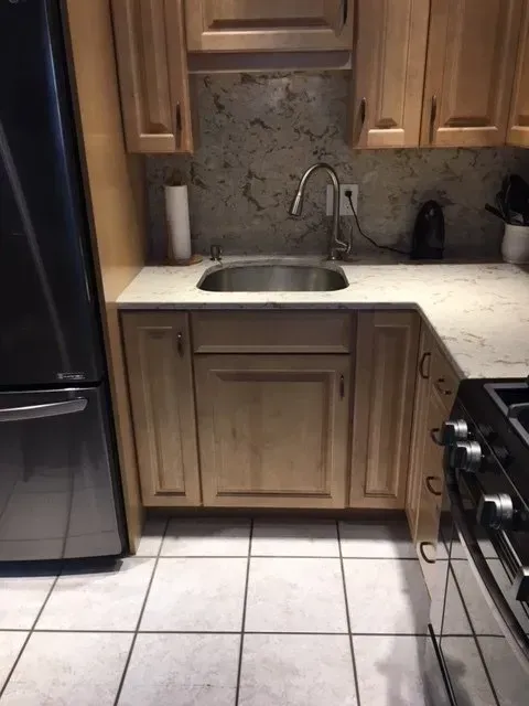 Kitchen sink with wood cabinets, stainless steel faucet, and granite backsplash.