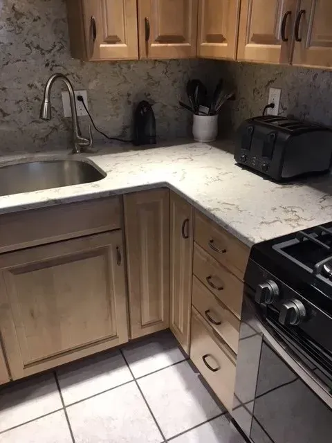 Kitchen corner with light wood cabinets, granite countertop, sink, and stove.