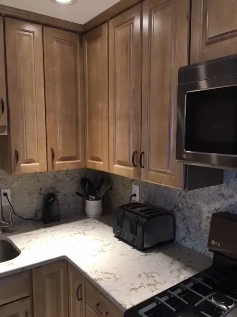 Kitchen corner with light brown cabinets, beige countertop, and a microwave.