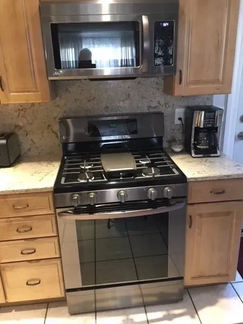 Stainless steel gas range and microwave in a kitchen with light wood cabinets and granite countertops.