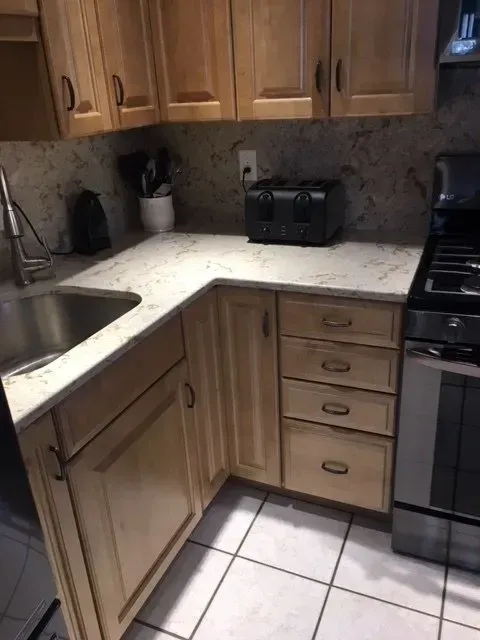 Kitchen with light wood cabinets, white countertop, sink, and a black toaster.