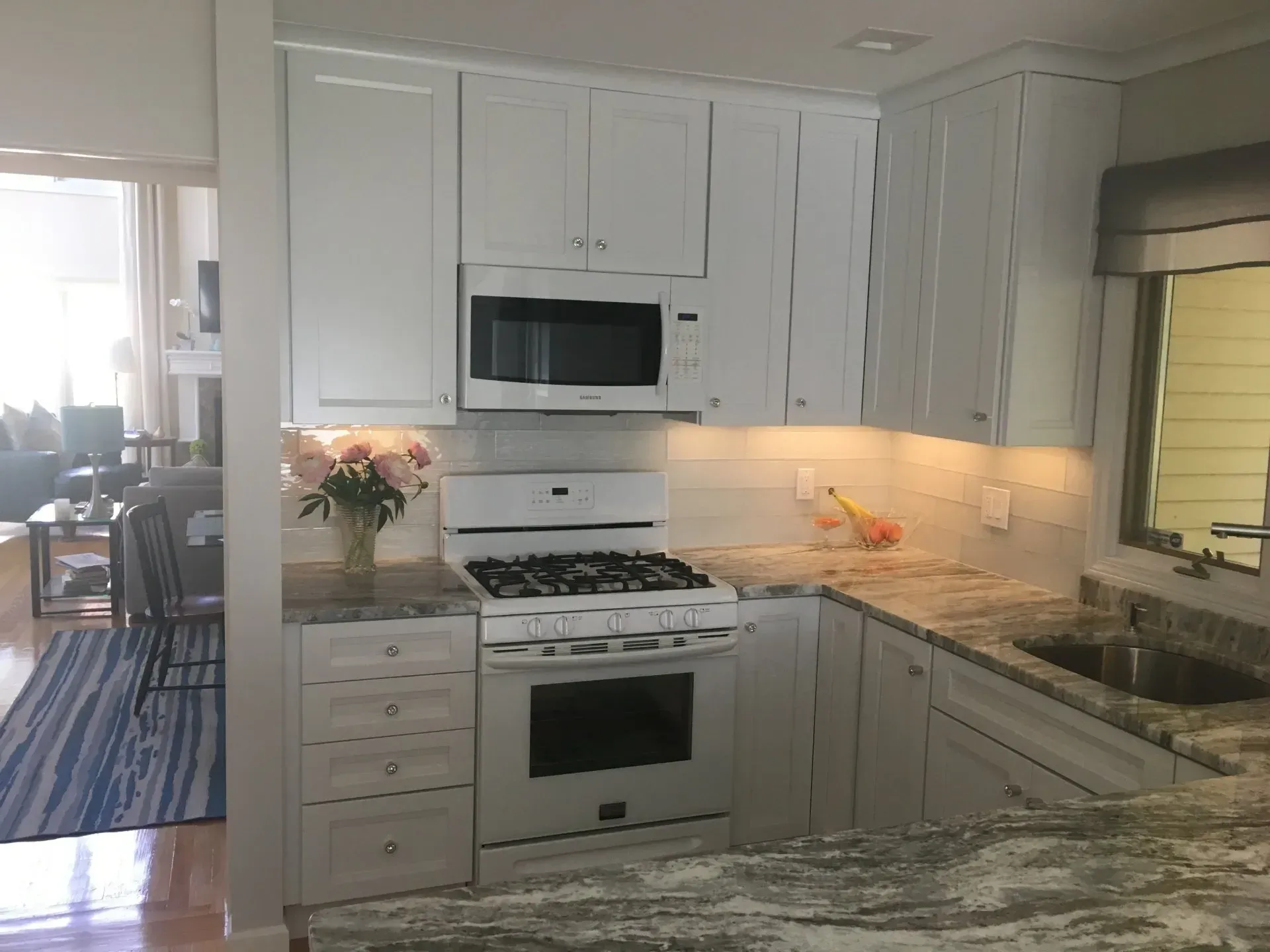 White kitchen with granite countertops, cabinets, appliances, and overhead lighting.