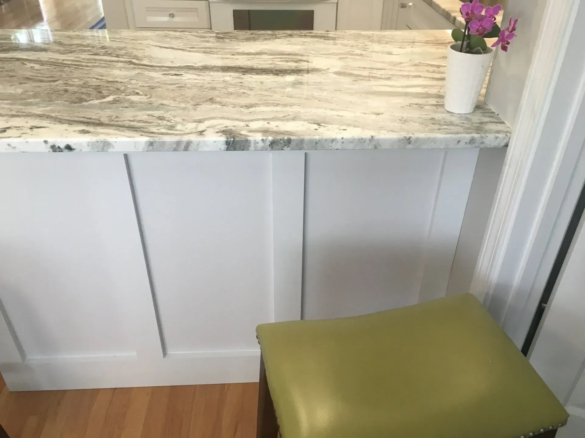 White kitchen island with granite countertop, green stool, and flowers.