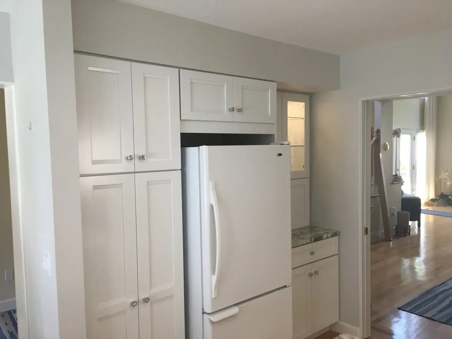 Kitchen with white cabinets, refrigerator, and countertop with a light gray wall.