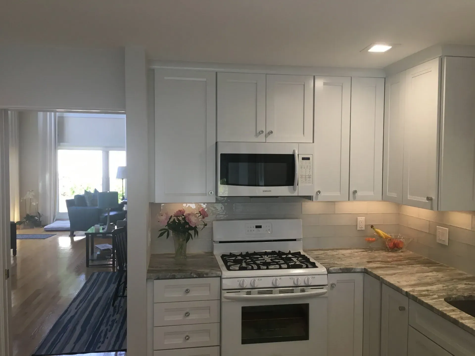 White kitchen with cabinets, microwave, stove, granite countertops. View into living room.
