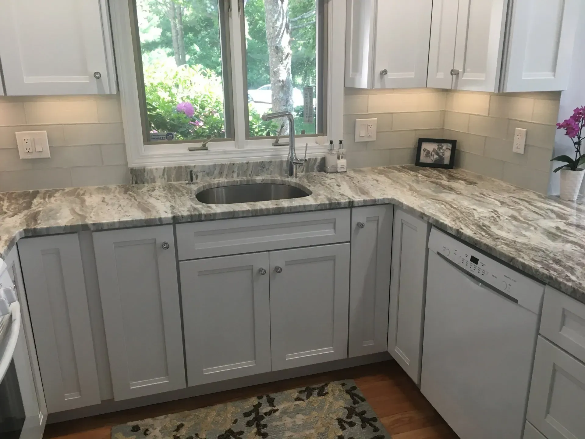 Kitchen with white cabinets, granite countertops, and a stainless steel sink, near a window.
