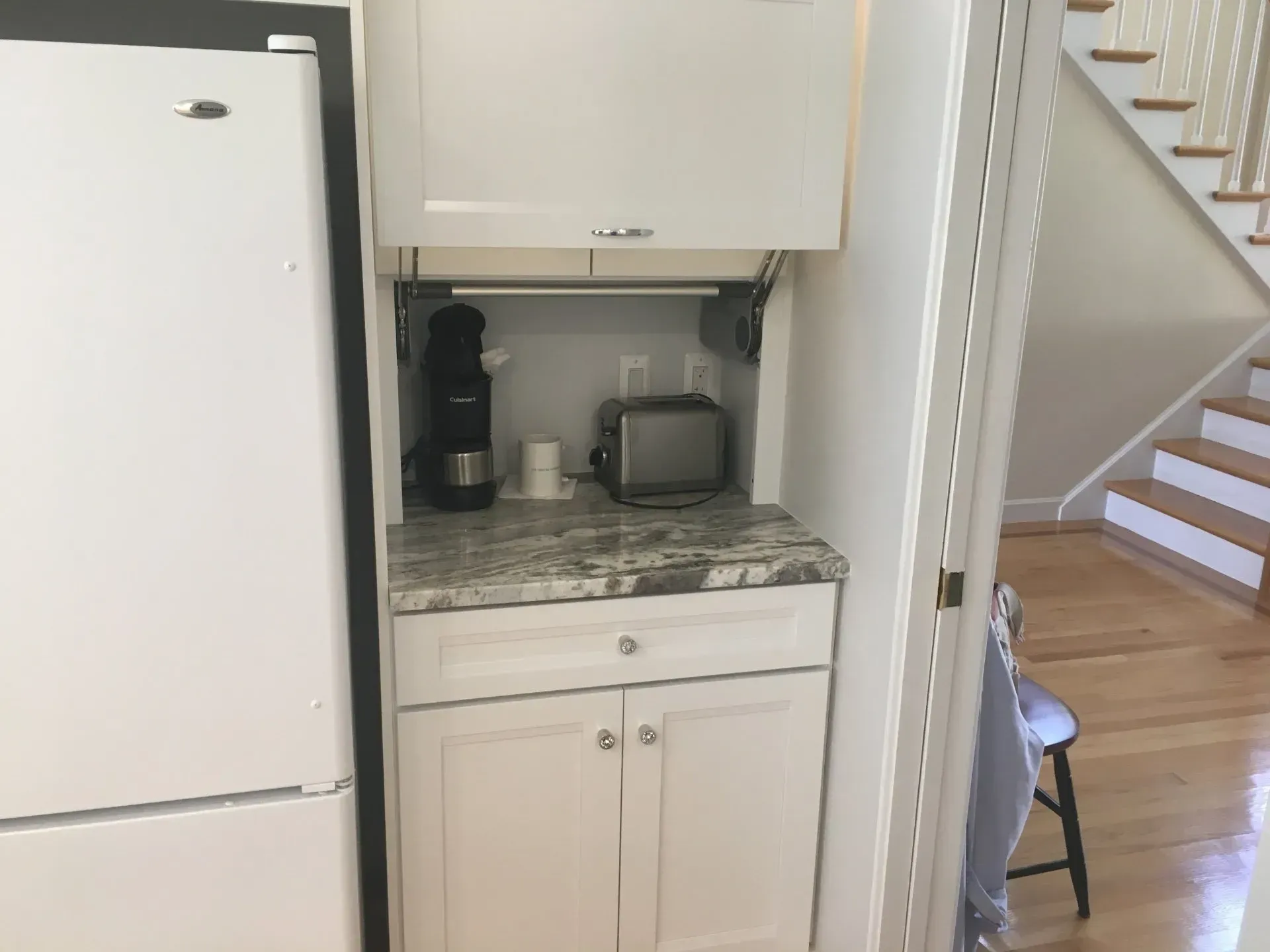 Built-in kitchen appliance cabinet with coffee maker, toaster, and granite countertop beside a white refrigerator.
