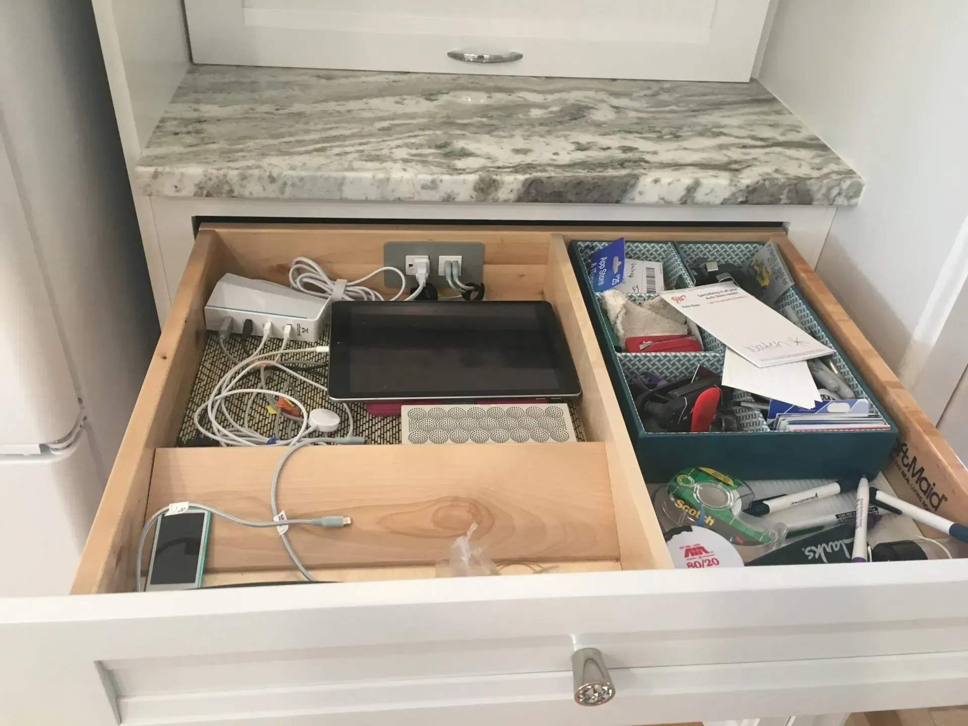 Open kitchen drawer with charging station, small tray, and miscellaneous items.