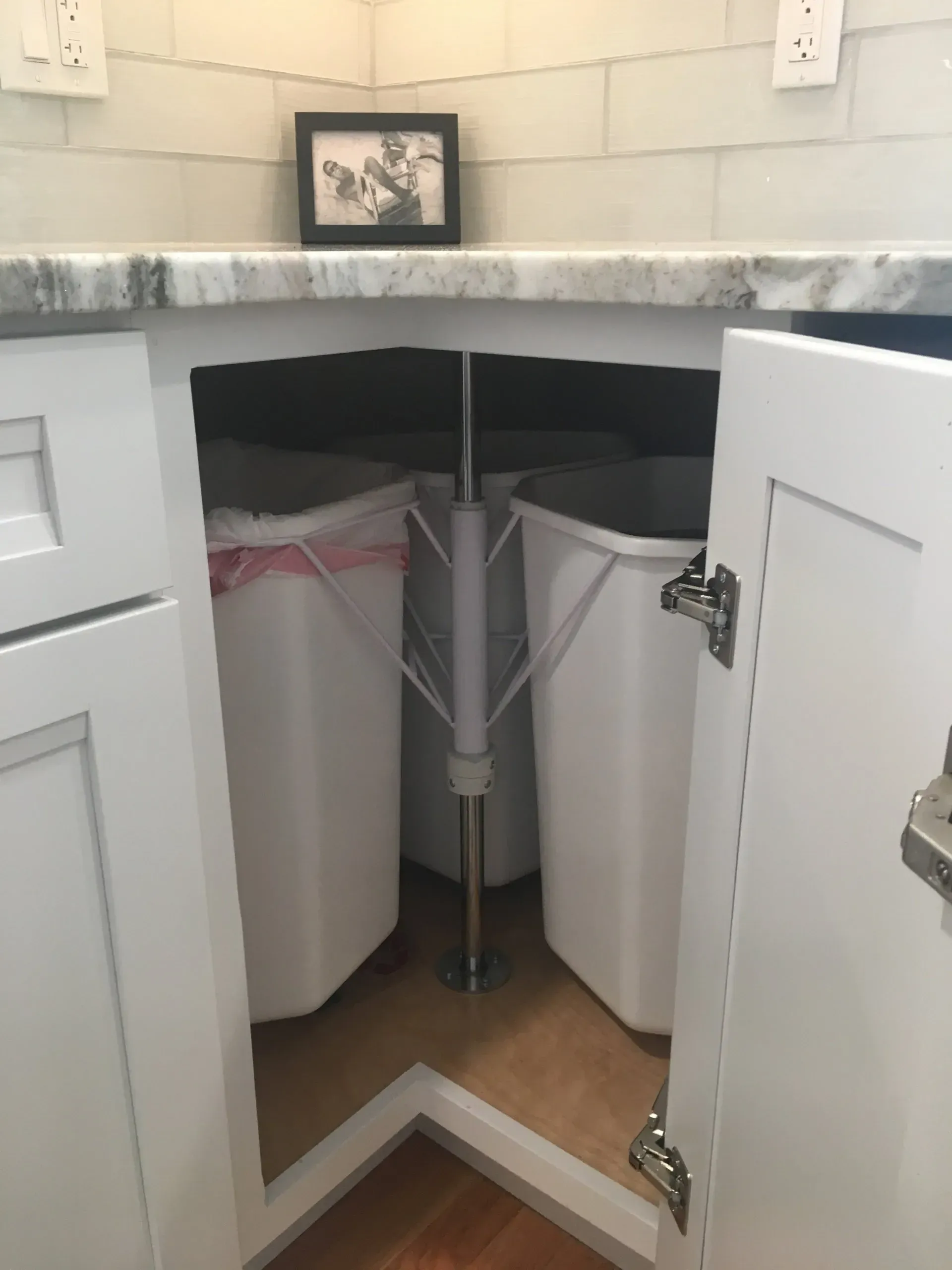 White kitchen cabinet with two pull-out trash bins, with a central pole.