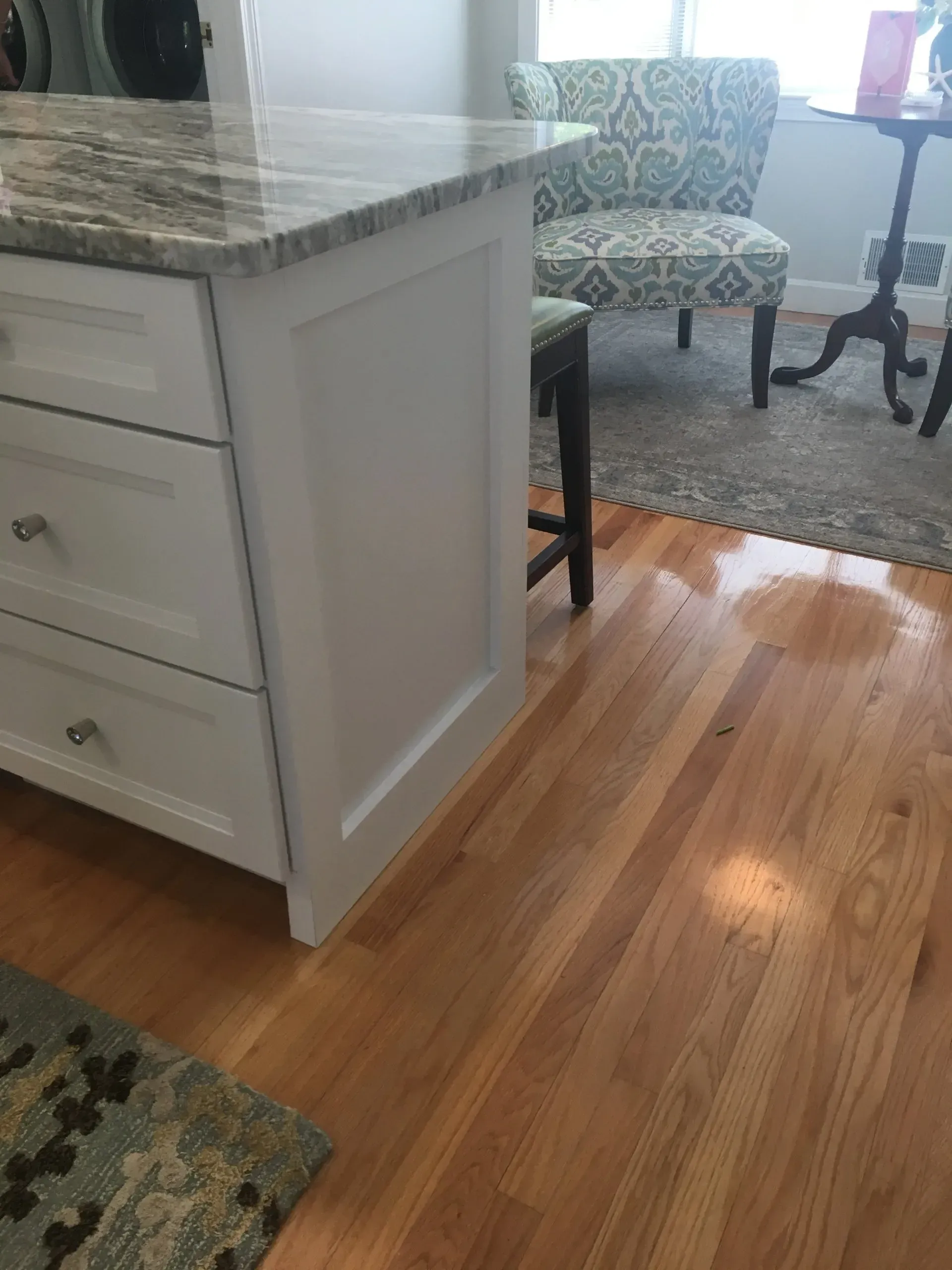 White kitchen island with granite countertop, white cabinets, hardwood floor, and chair.