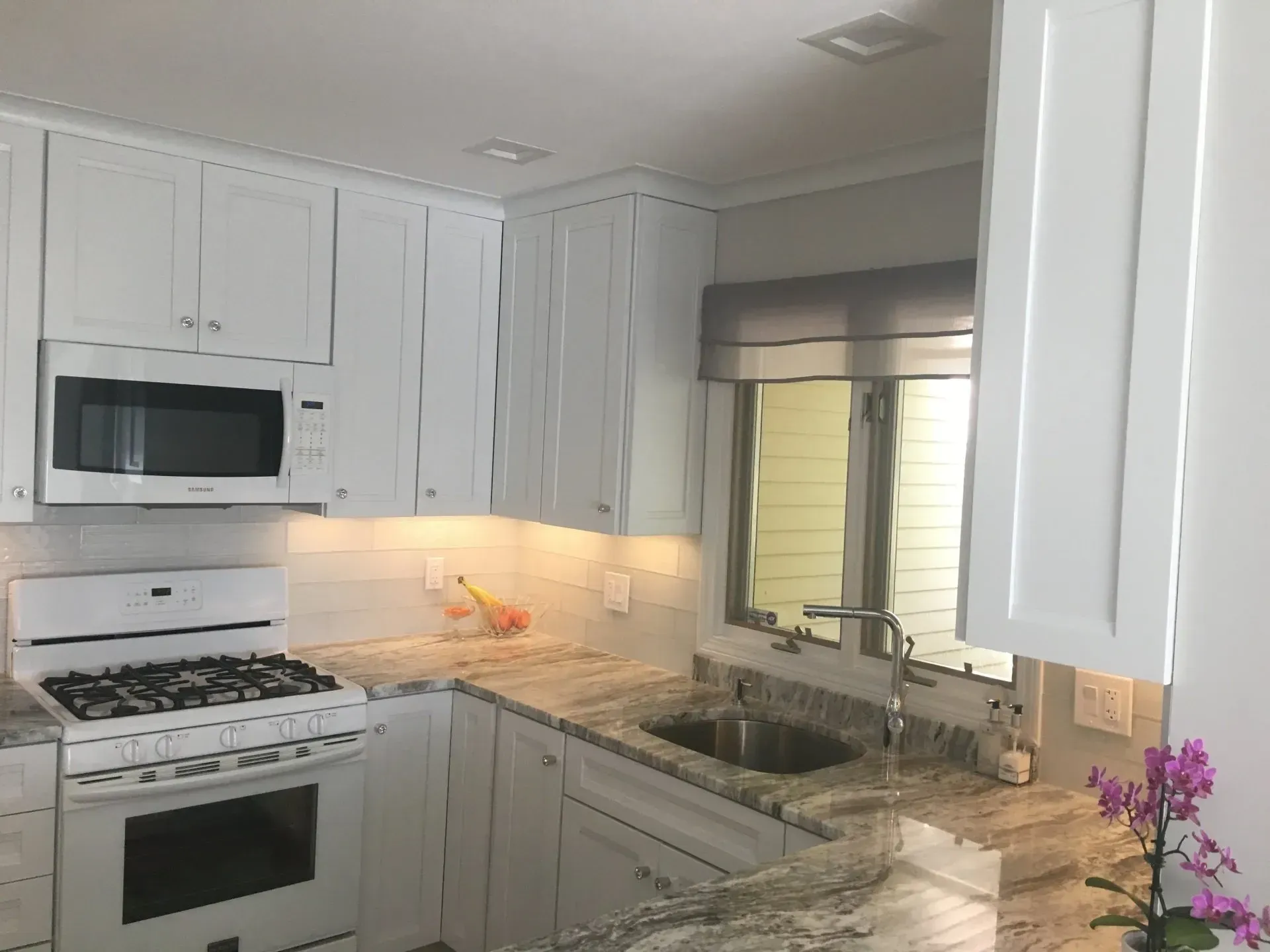 White kitchen with stove, microwave, cabinets, and granite countertop.