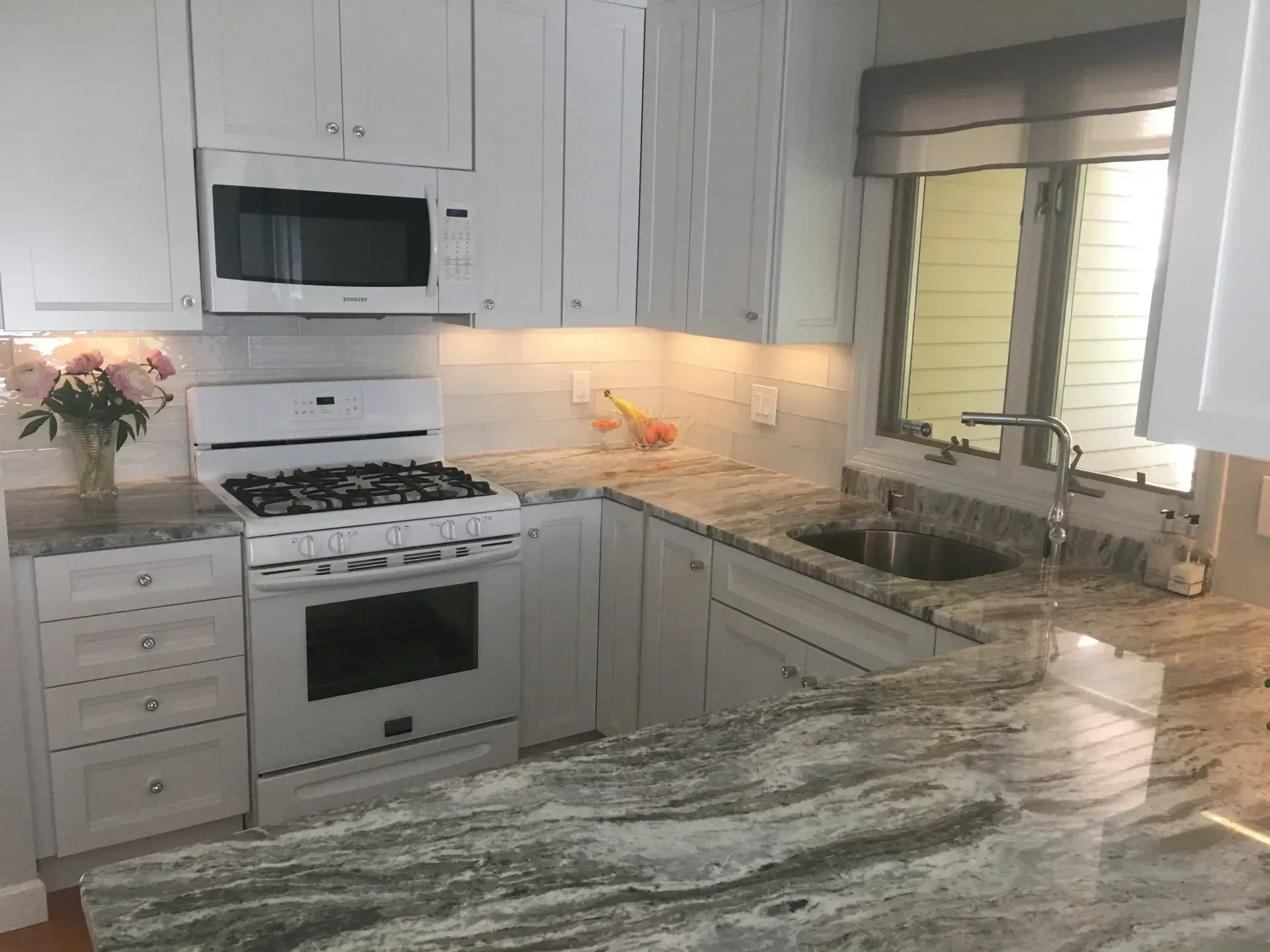 White kitchen with granite countertops, stainless steel sink, and microwave over stove.
