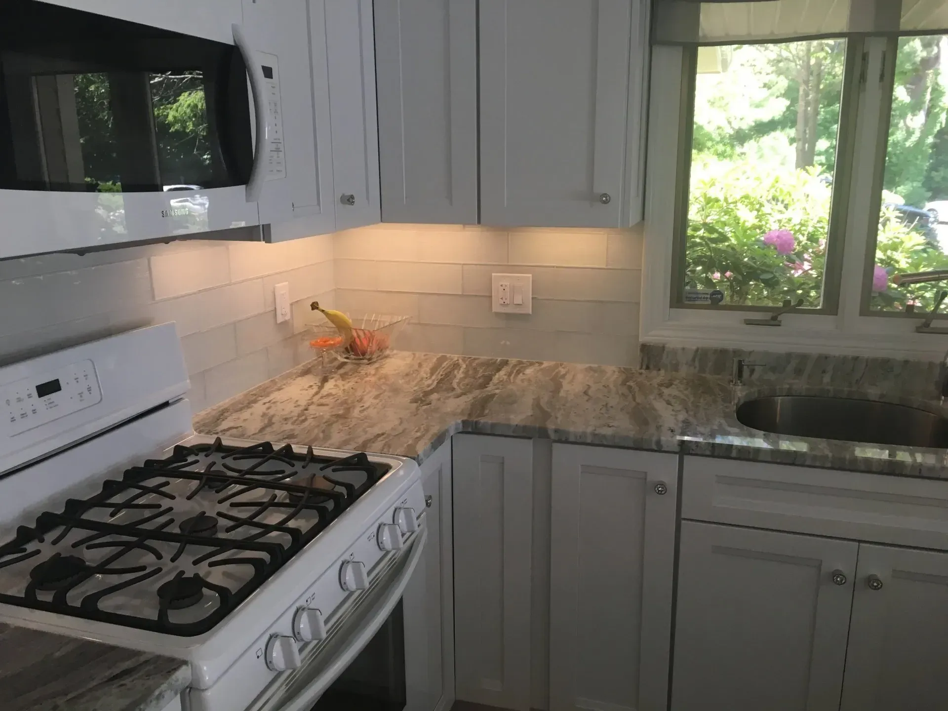 Kitchen corner with white cabinets, light countertop, range, and window to a backyard.