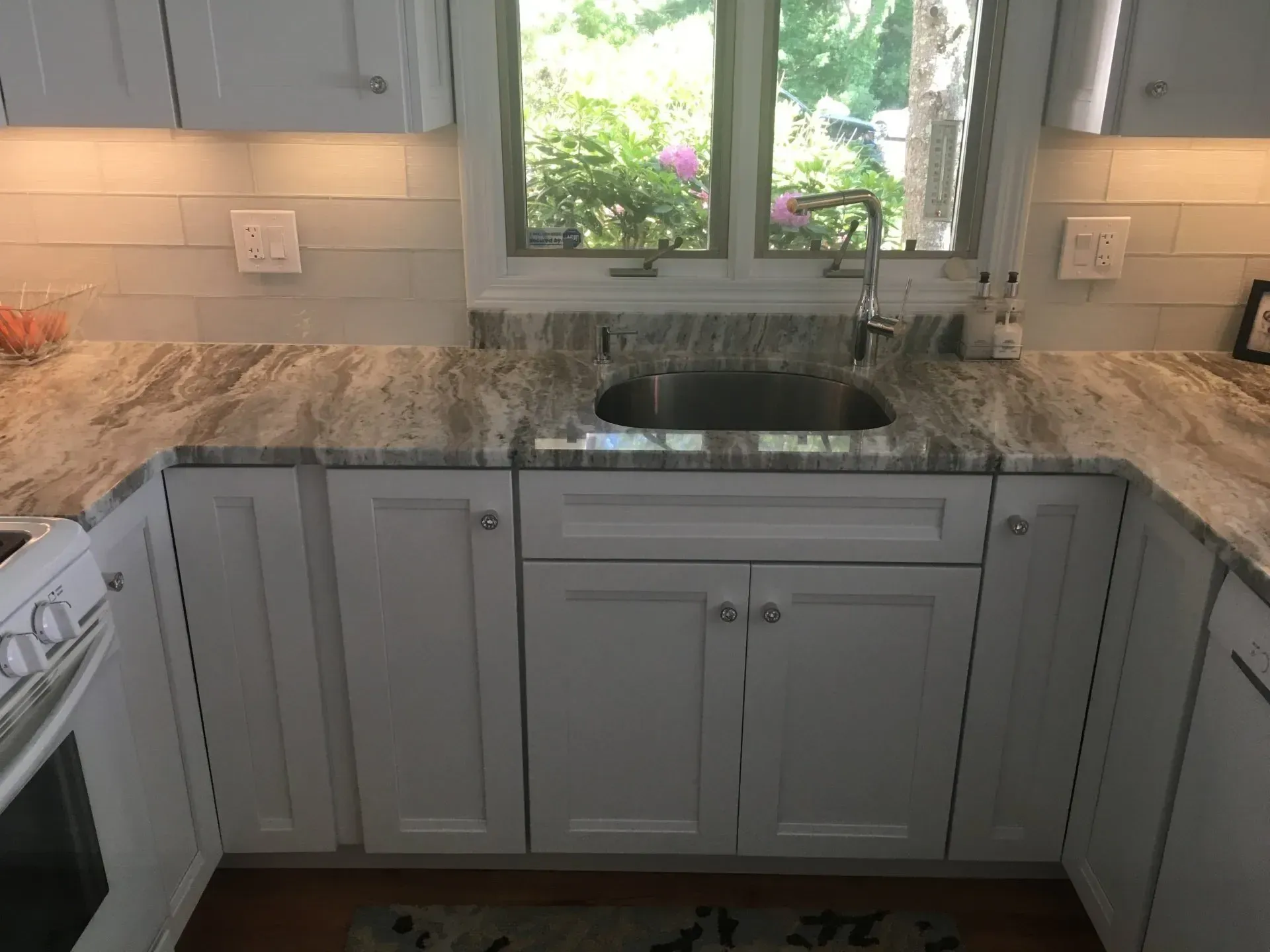White kitchen cabinets with granite countertop, sink under a window.