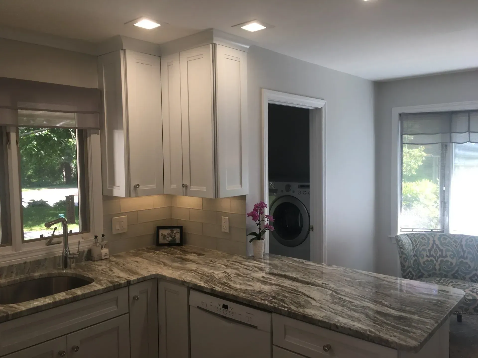 Kitchen with white cabinets, granite countertops, and a washing machine visible through a doorway.