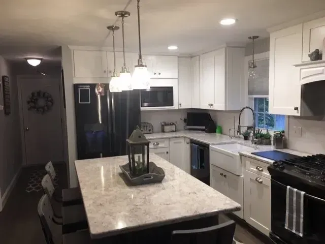 Modern white kitchen with island, black appliances, pendant lights, and light countertops.
