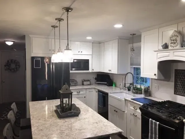 Modern white kitchen with island, black appliances, pendant lights, and light countertops.
