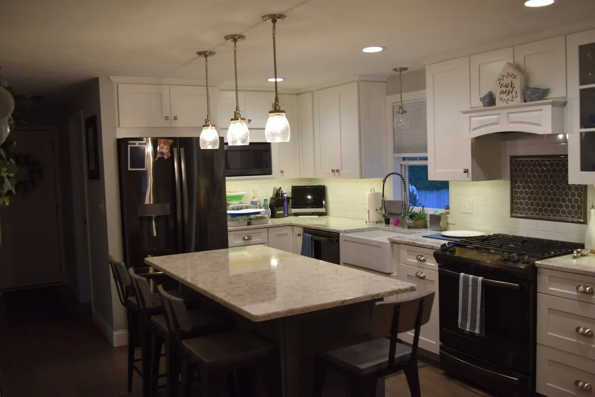 Kitchen with white cabinets, dark island, stainless steel appliances, and pendant lights.