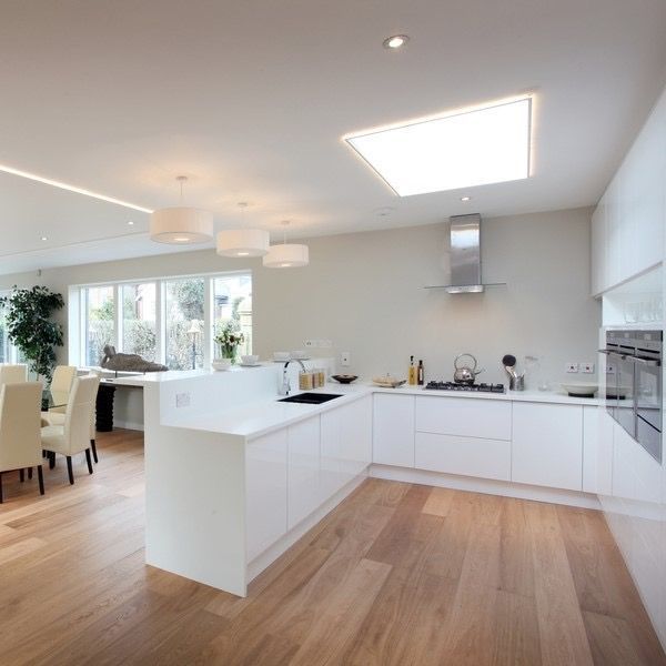 Modern white kitchen with wooden floors, island, dining area, and large window.