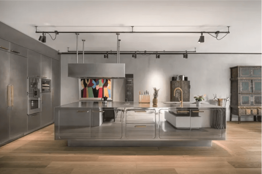 Modern stainless steel kitchen with large island, track lighting, and wood floors.