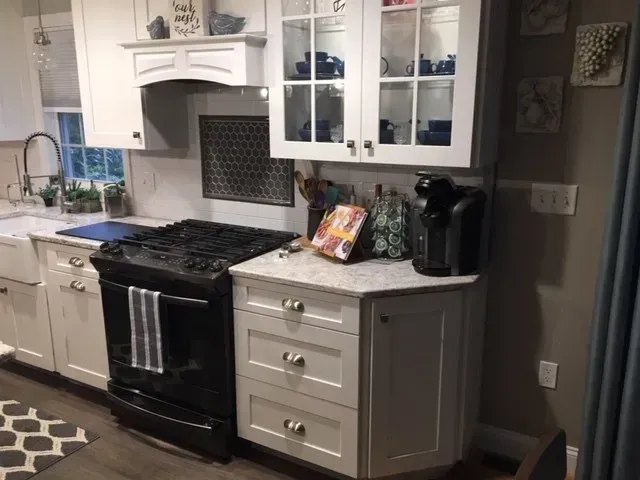 White kitchen with black stove, light countertops, and cabinet with coffee maker.