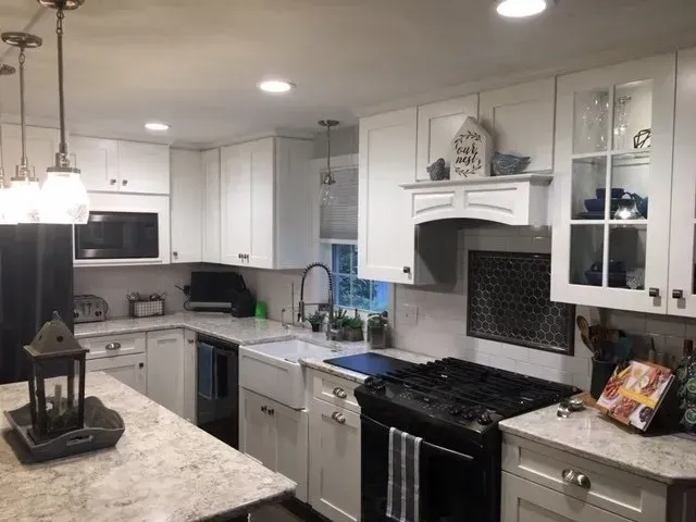 White kitchen with granite countertops, black appliances, and pendant lights.