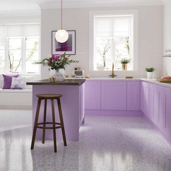 Lavender kitchen with island, cabinets, and speckled floor. Windows and a stool are also present.