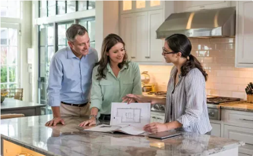 A man showing documents to two women in a kitchen with a large island and cabinets.