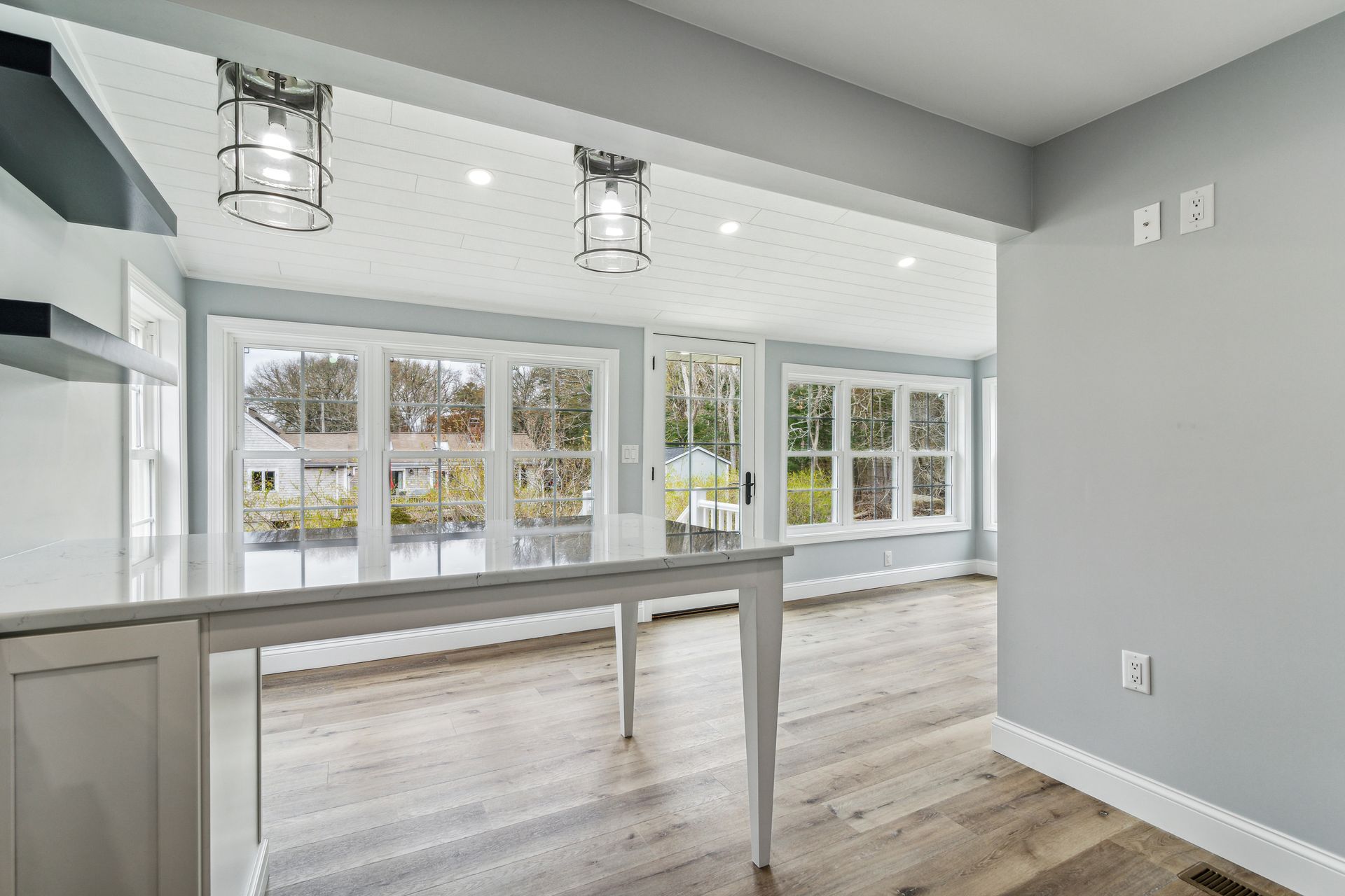 Modern kitchen with light gray walls, white trim, and hardwood floors. A table with windows facing the exterior.
