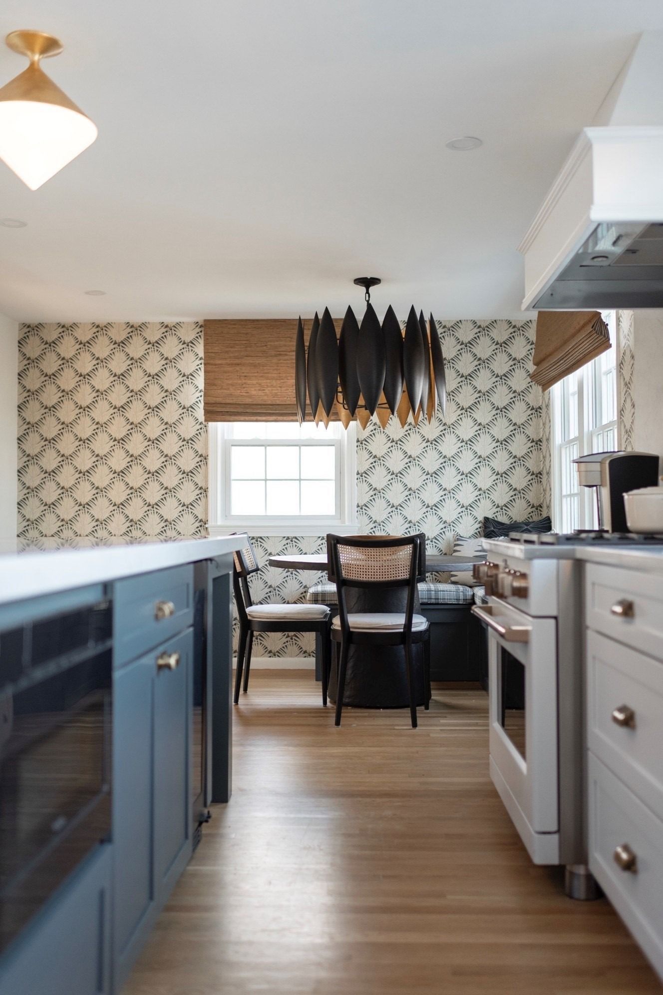 Kitchen with blue island, patterned wallpaper, black chandelier, and wood flooring.
