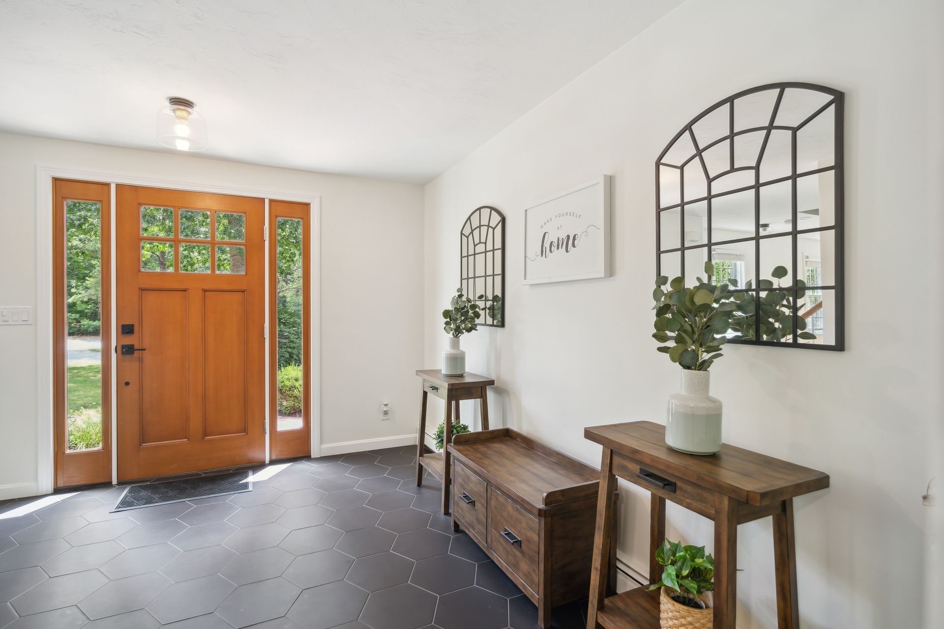Wooden front door and entryway with console tables, mirrors, and greenery.