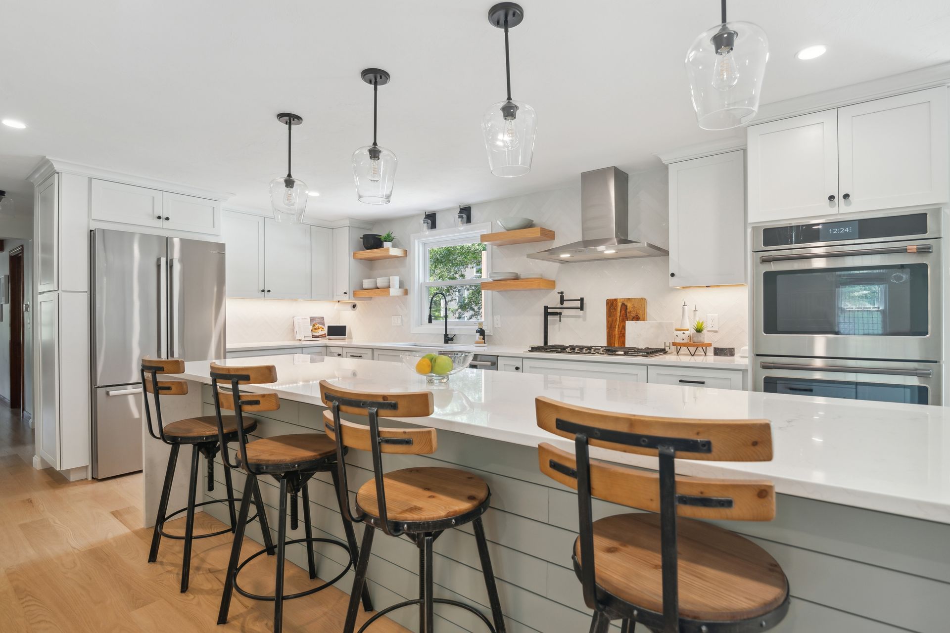 Modern white kitchen with a stainless steel refrigerator, island seating, and pendant lights.