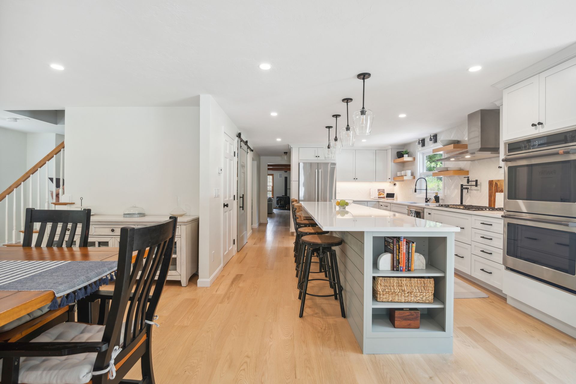 Modern kitchen with island, seating, and stainless steel appliances. Bright, with light wood floors.