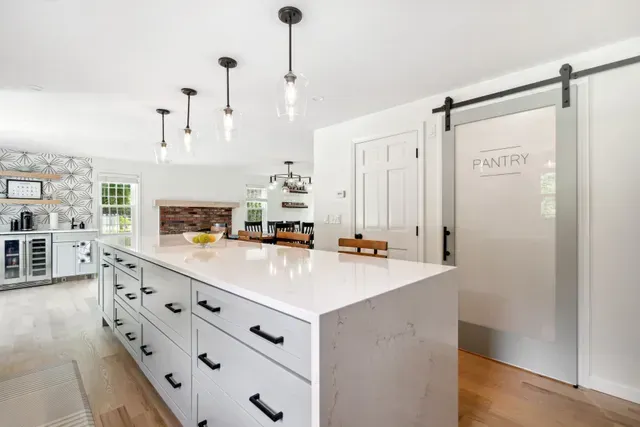 Modern white kitchen with island, pendant lights, and sliding barn door pantry Cape Cod MA