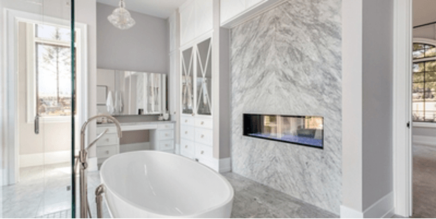 Elegant white bathroom with marble accent wall, fireplace, and freestanding tub.