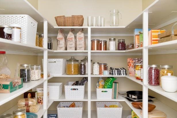 A well-organized pantry with white shelves, filled with labeled jars, baskets, and packages of food.