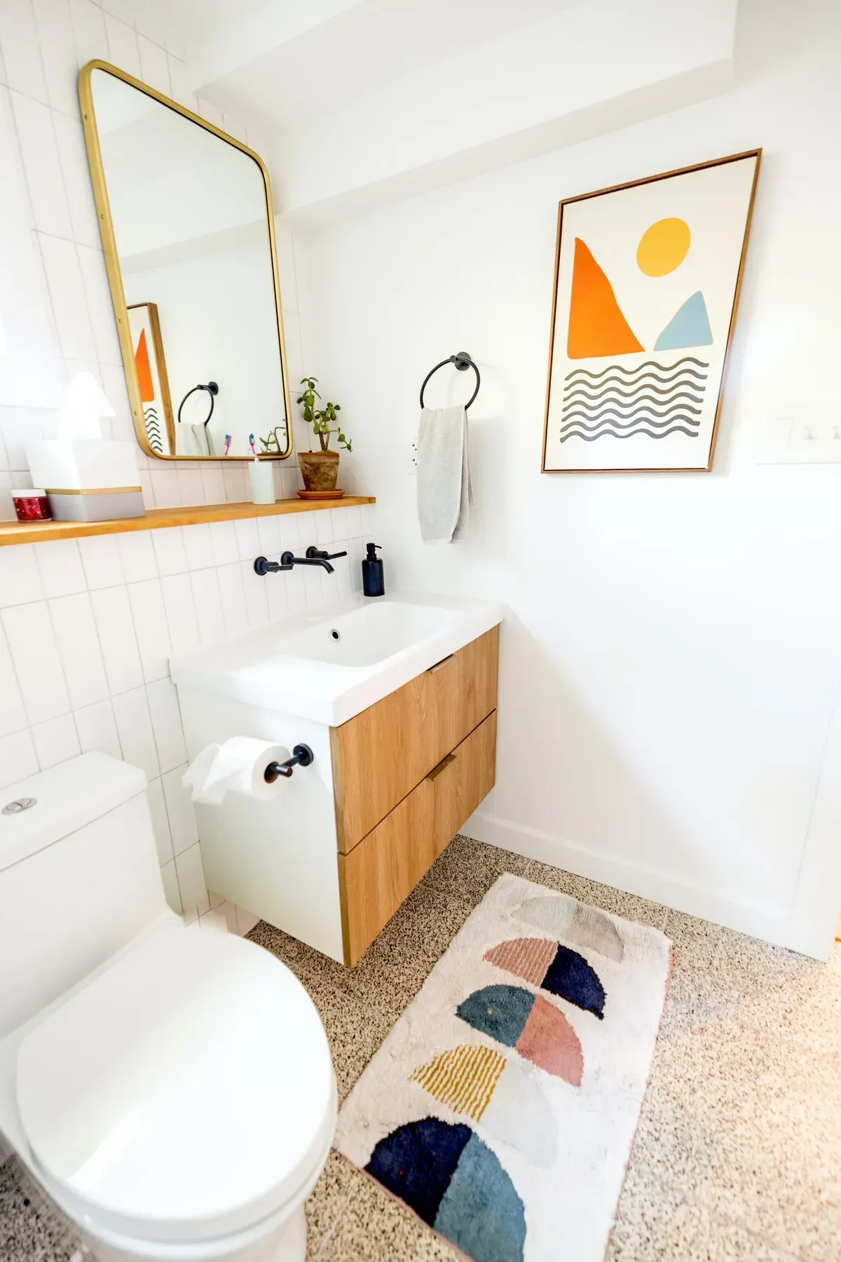 Modern bathroom with a wooden vanity, gold mirror, and colorful abstract art.