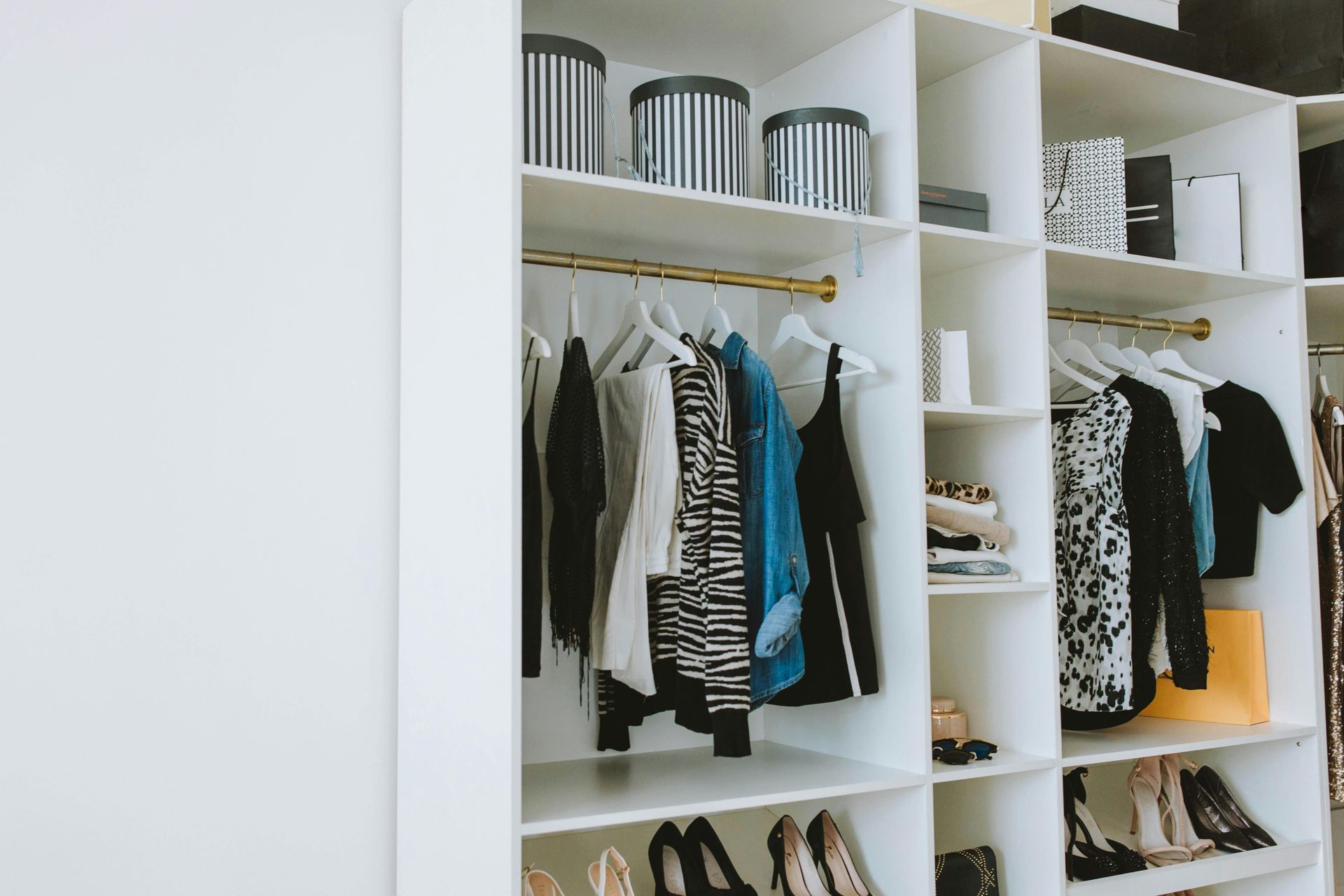 White closet with clothes hanging, shoes and boxes.