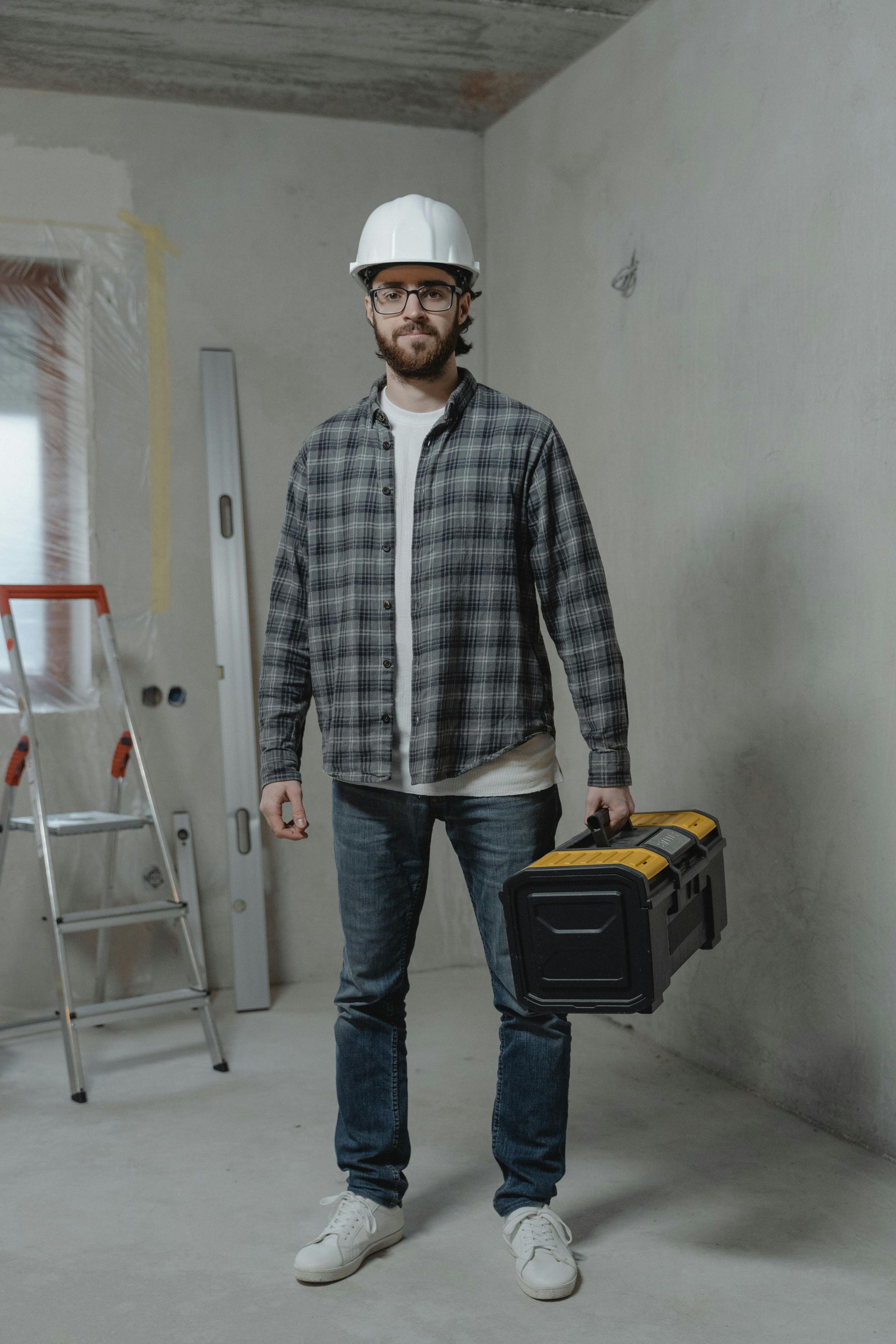 Construction worker in hard hat holding toolbox, standing in unfinished room.